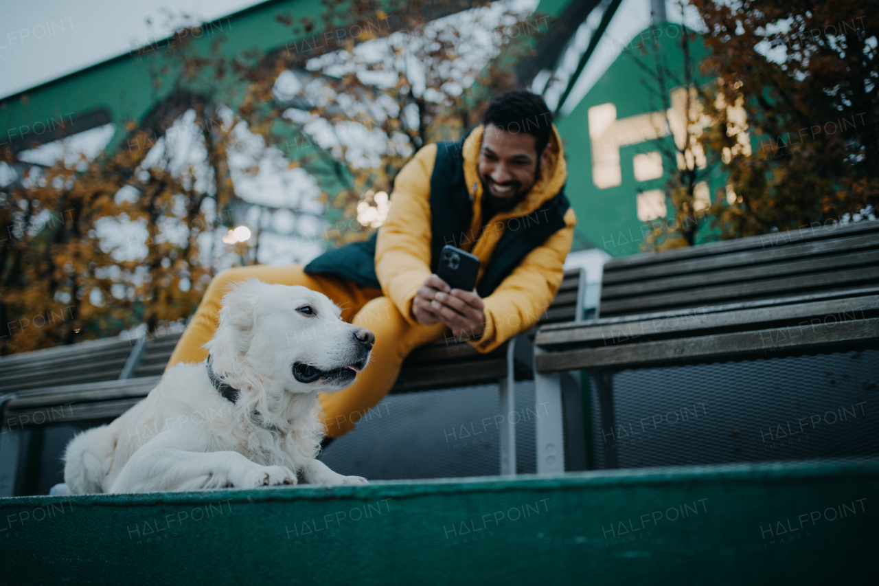 Happy young man resting and taking a foto of his dog in urban city area in autumn day.