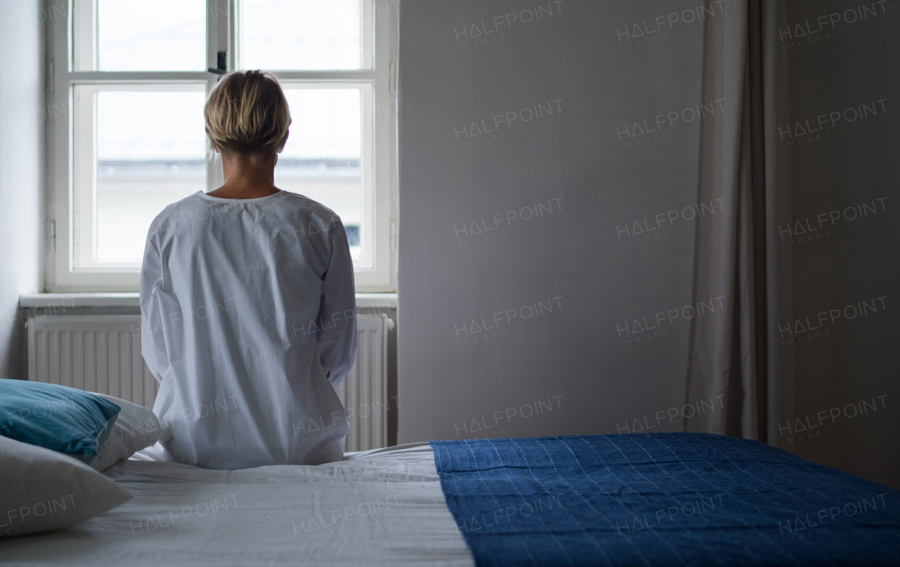 Rear view of woman patient sitting on bed in hospital feeling stressed, mental health and coronavirus concept. Copy space.