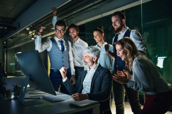 A group of business people with computer in an office in the evening, expressing excitement.