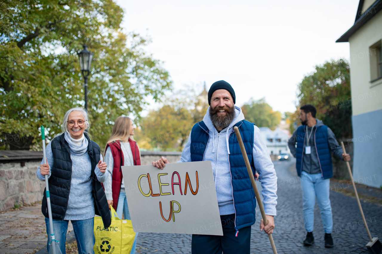 A diverse group of happy volunteers walking with banner and tools to do street clean up.