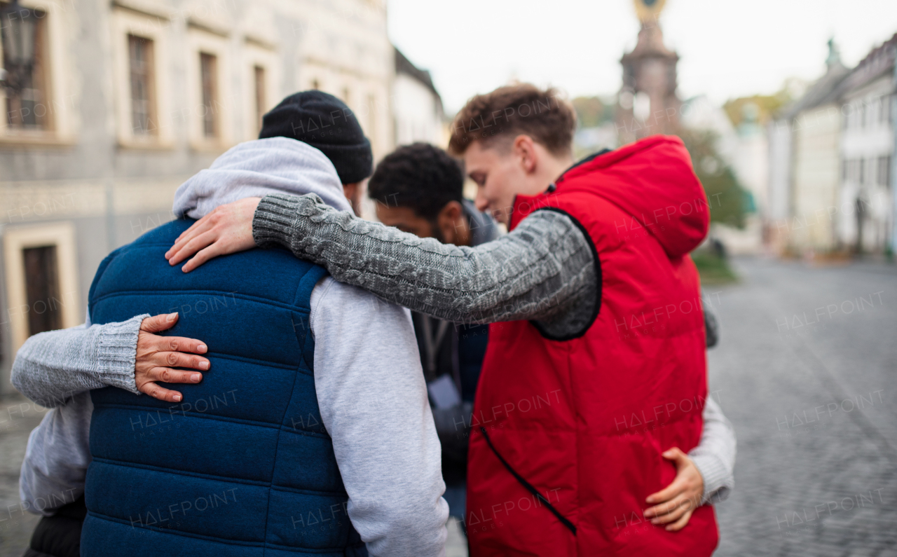 A rear view of community service volunteers hugging together outdoors in street