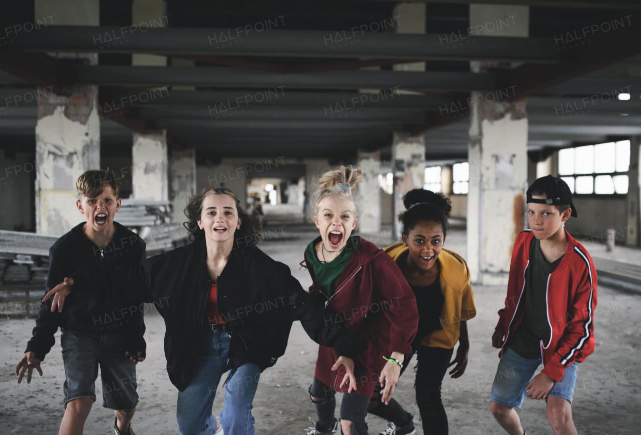 Front view of group of teenagers girl gang standing indoors in abandoned building, shouting at camera.