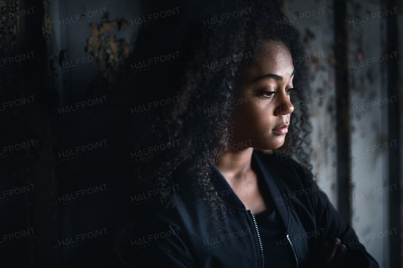 Side view portrait of sad mixed- race teenager girl standing indoors in abandoned building.