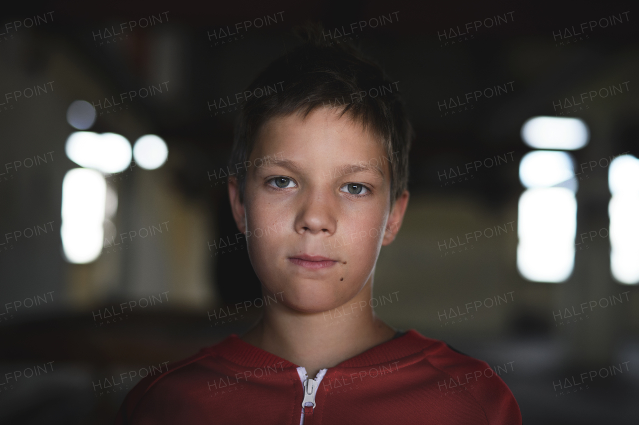 Sad and disappointed teenagers boy standing on chair indoors in abandoned building, looking at camera.