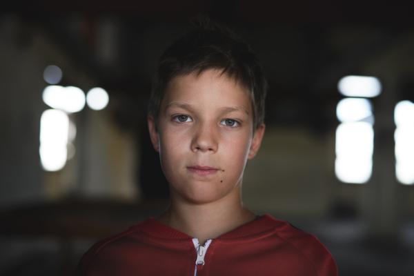 Sad and disappointed teenagers boy standing on chair indoors in abandoned building, looking at camera.
