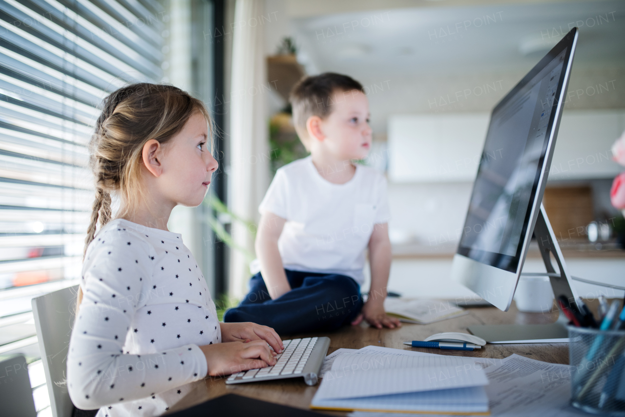 Small girl and boy sitting at the table, using computer indoors at home. Corona virus and quarantine concept.