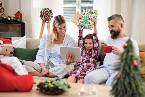 Family with small daughter indoors at home at Christmas, having video call on tablet.