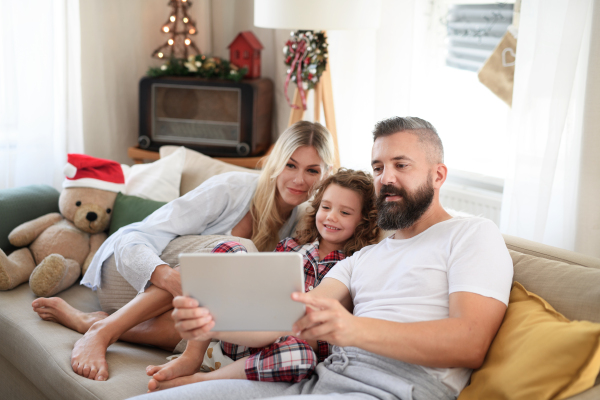 Family with small daughter indoors at home at Christmas, having video call on tablet.
