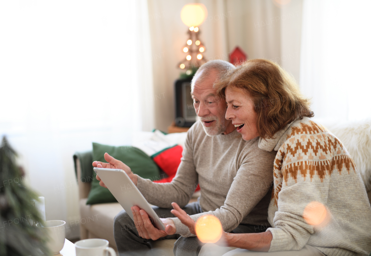 Side view of happy senior couple indoors at home at Christmas, having video call with family.