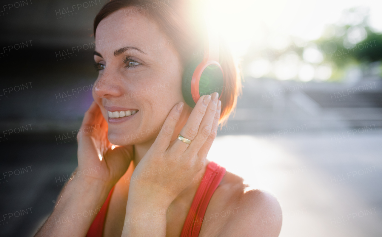 A close-up of young woman runner with headphones in city, listening to music and resting.