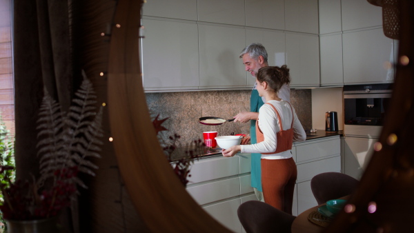 A teenage daughter with her father cooking in kitchen together.