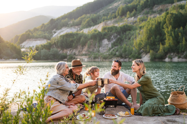 A happy multigeneration family on summer holiday trip, barbecue by lake.