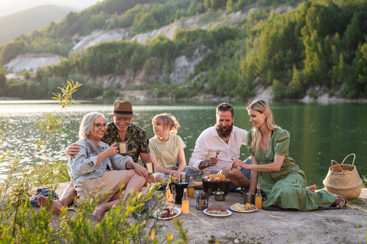 A happy multigeneration family on summer holiday trip, barbecue by lake.
