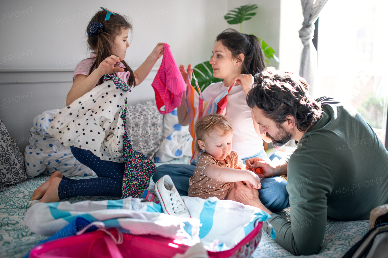 Portrait of family with two small daughters packing for holiday on bed at home.