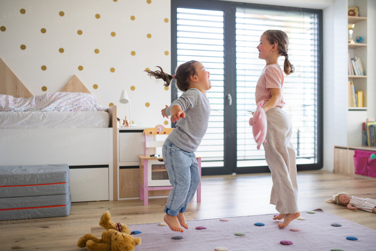 A portrait of girls sisters playing indoors at home, jumping.
