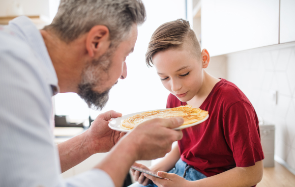 A mature father with small son indoors in kitchen, making pancakes.