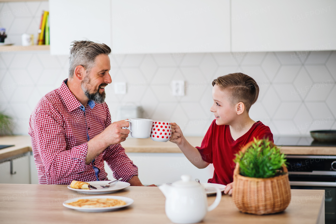 A mature father with small son indoors sitting at the table, eating pancakes.