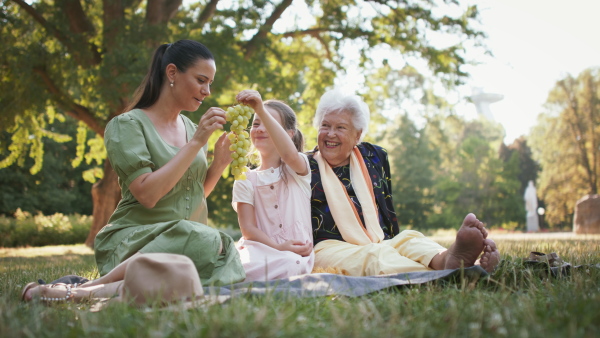 A small girl with mother and grandmother resting in a park, having picnic.