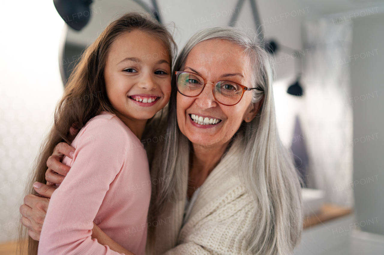 A senior grandmother and granddaughter standing indoors in bathroom, hugging and looking at camera.