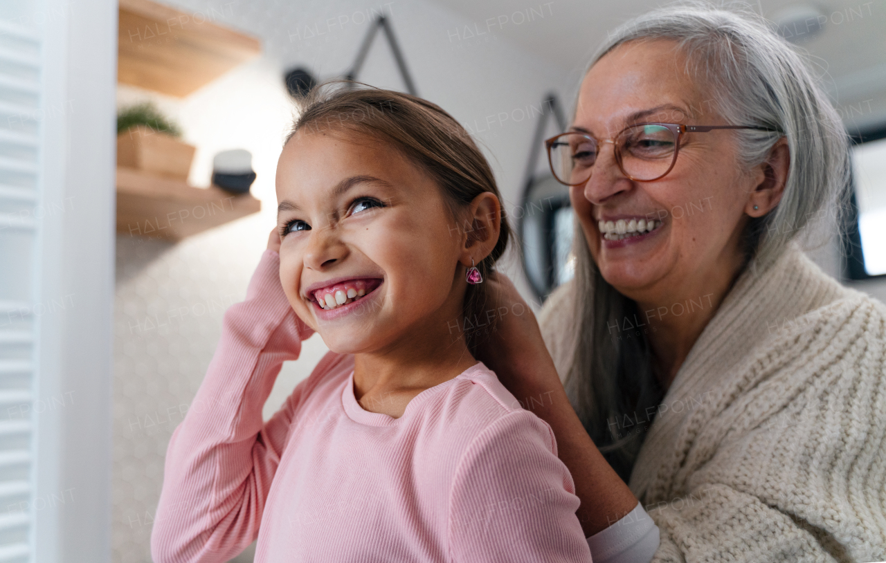 A senior grandmother and granddaughter standing indoors in bathroom, daily routine concept.