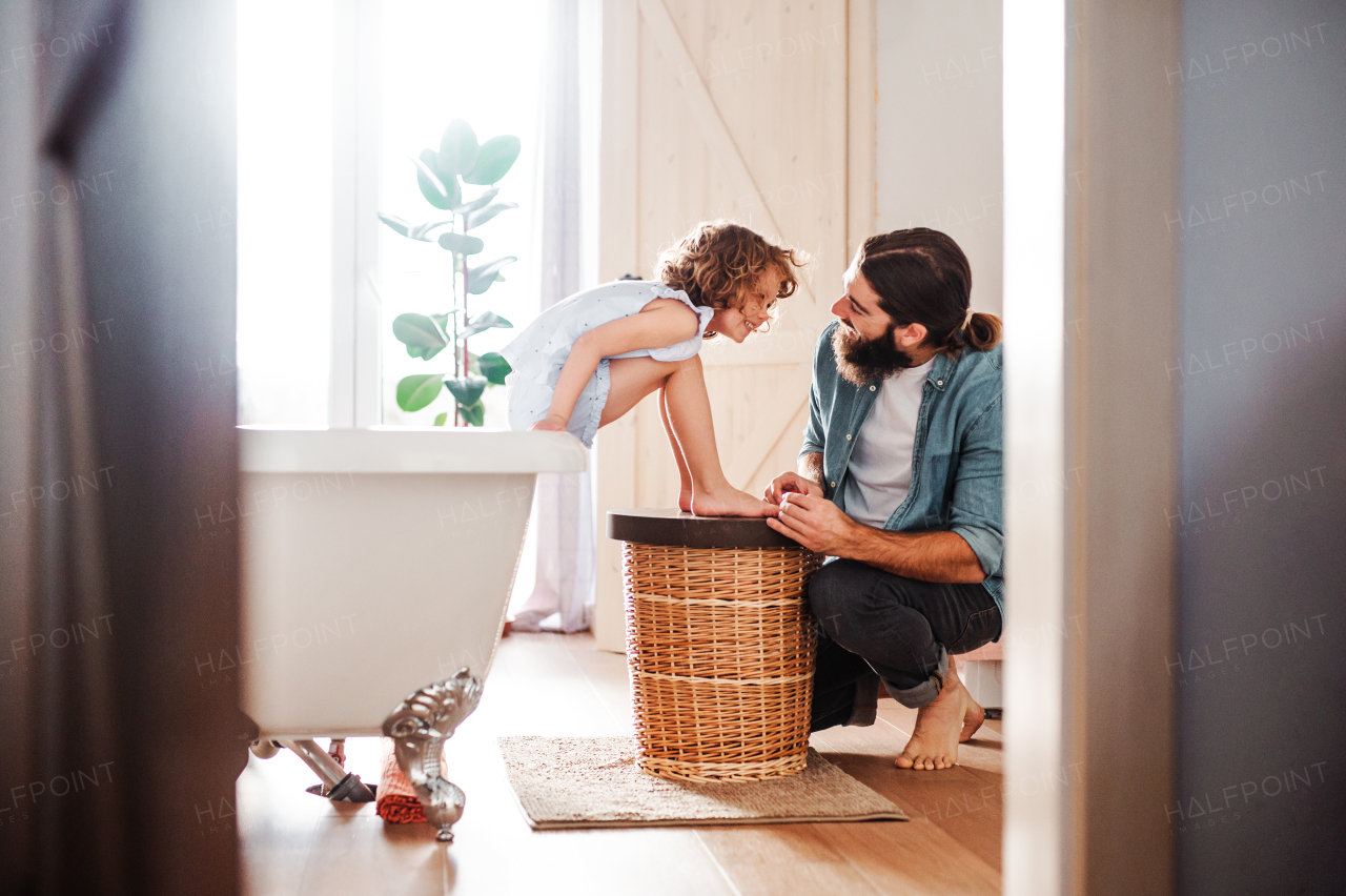 A young father painting small daughter's nails in a bathroom at home.