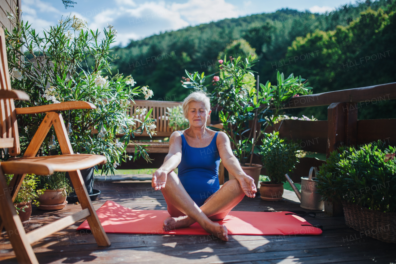 A senior woman sitting outdoors on a terrace in summer, doing yoga exercise. Copy space.