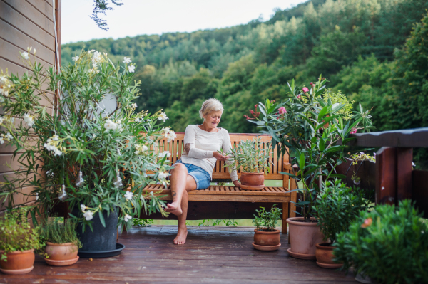 A happy senior woman sitting outdoors on a terrace in summer, resting.