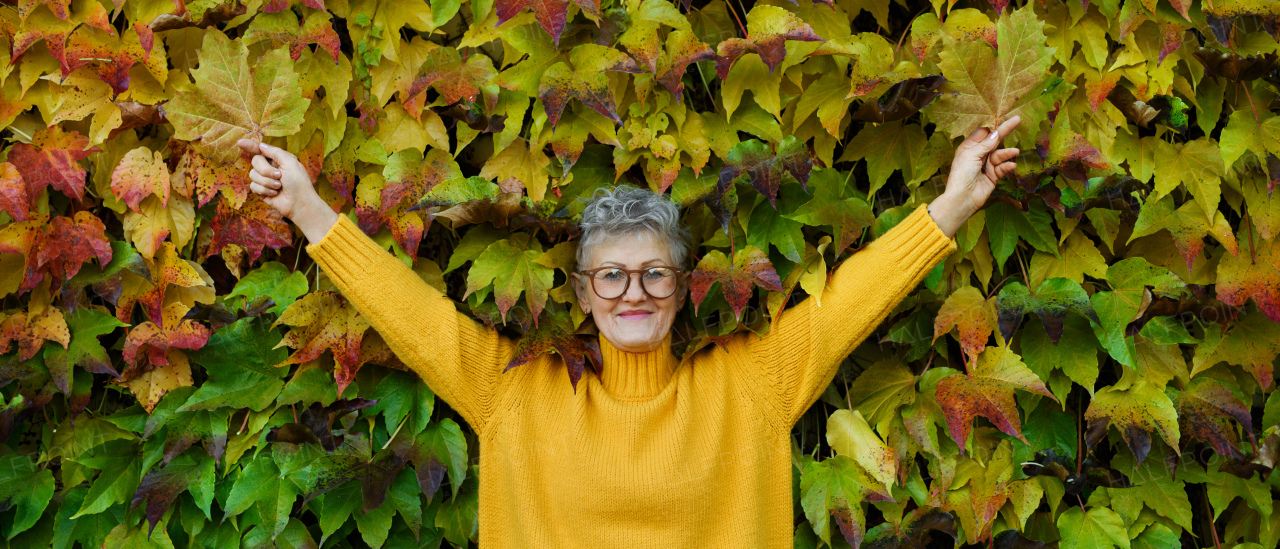 Portrait of senior woman standing outdoors against colorful natural autumn background, stretching arms.