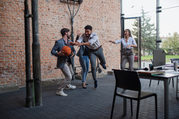 A group of cheerful young businesspeople playing basketball in office, taking a break concept.