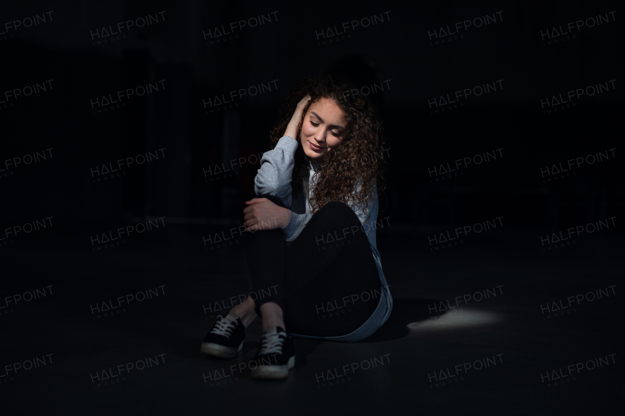 A portrait of happy young woman standing indoors against black bacground.