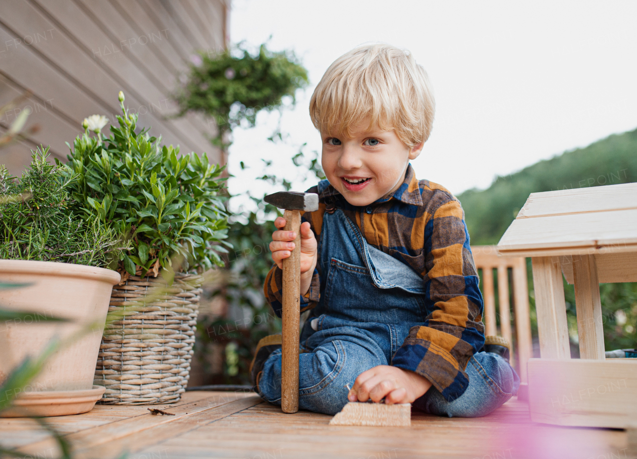 Portrait of happy small boy outdoors on table constructing birdhouse, diy project.