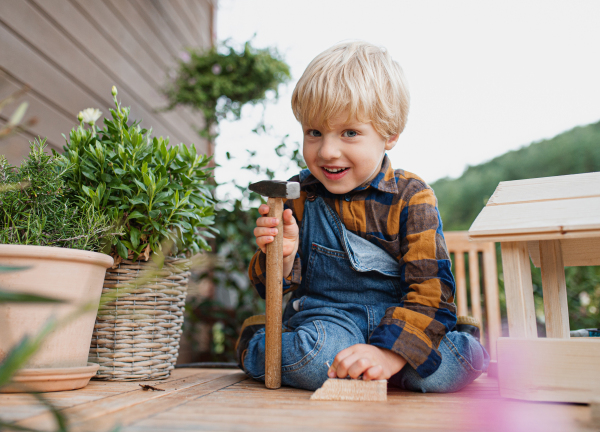 Portrait of happy small boy outdoors on table constructing birdhouse, diy project.