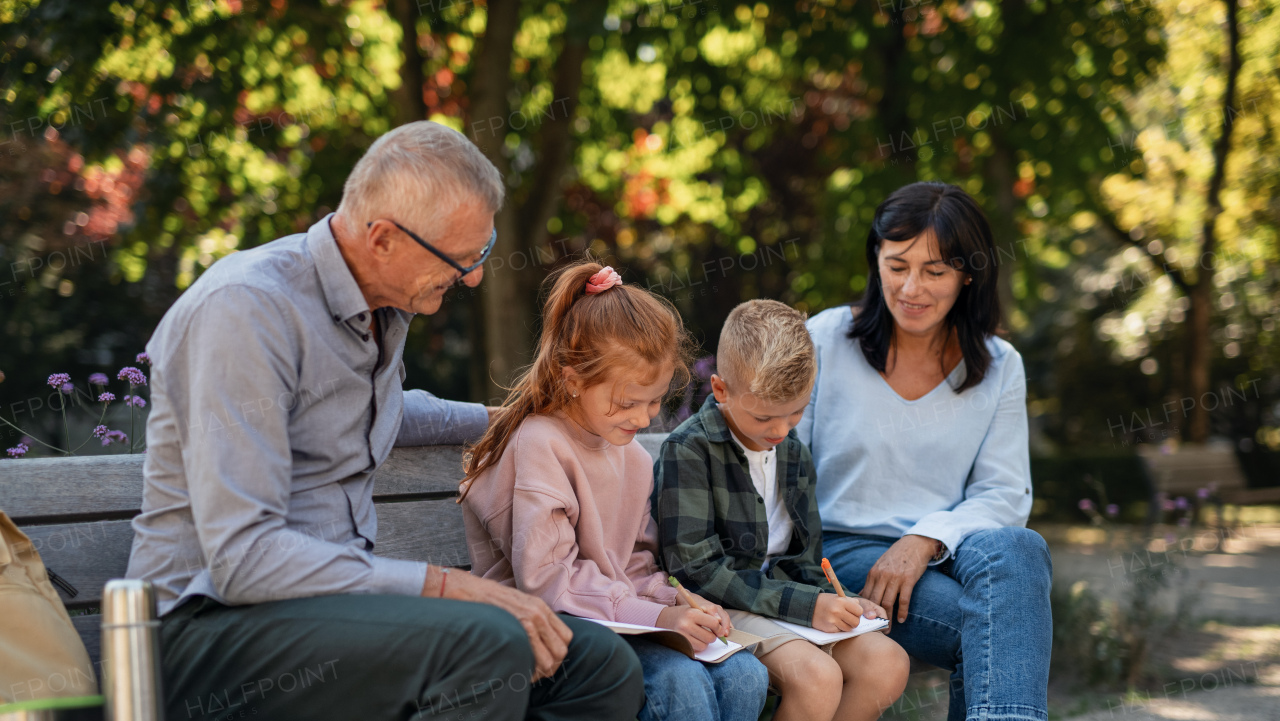 A senior couple with grandchildren sitting on bench and doing homewrok outdoors in park.