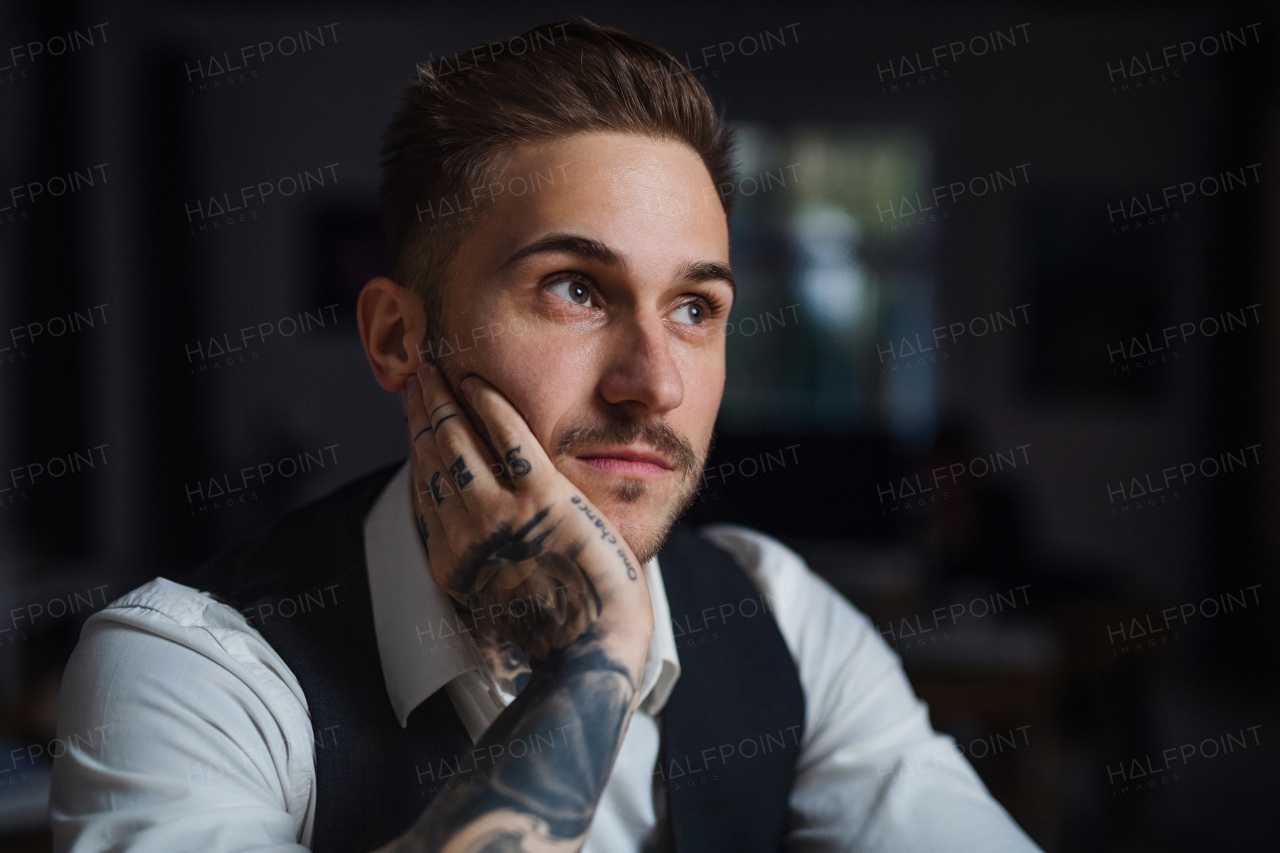 A front view of tired young businessman indoors in office, working late.