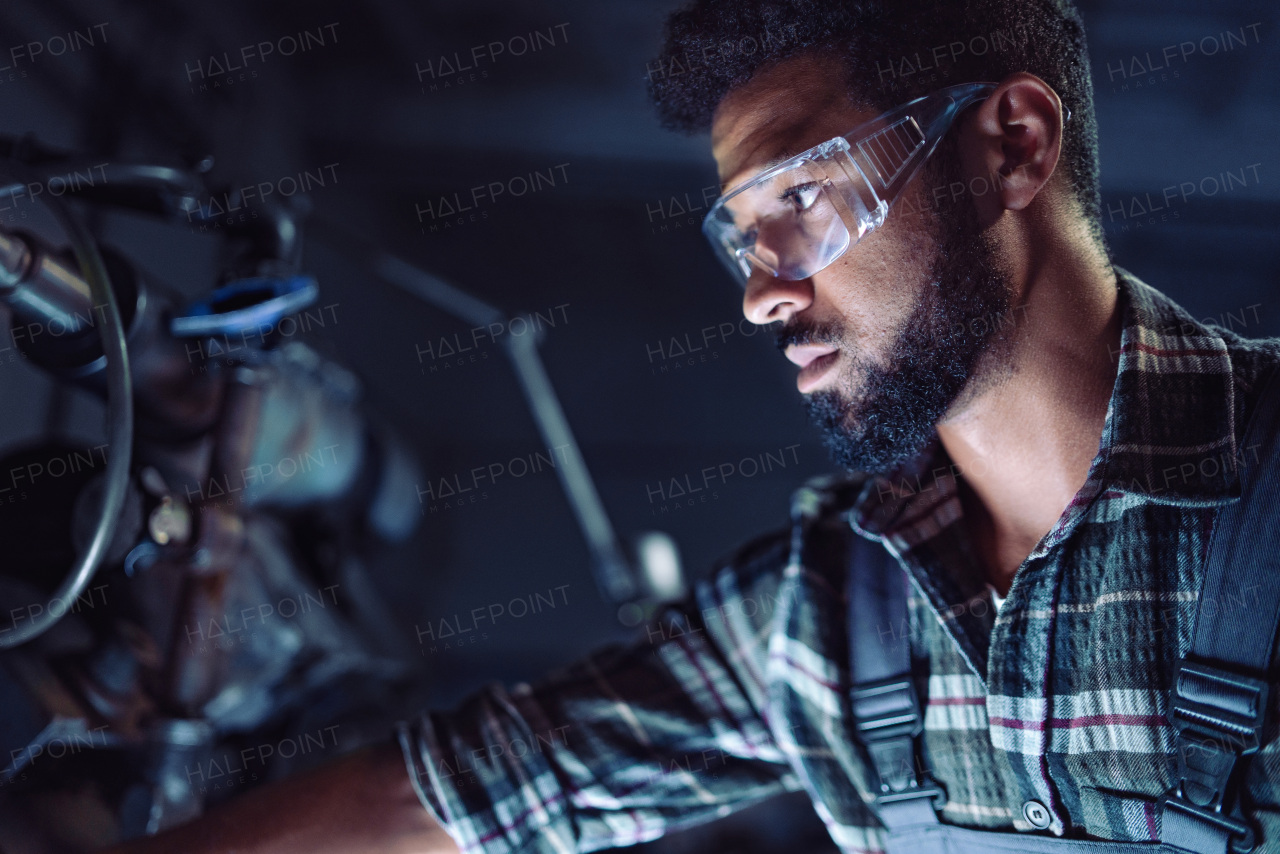 A close up of young concentrated african american industrial man working on cutter indoors in metal workshop.