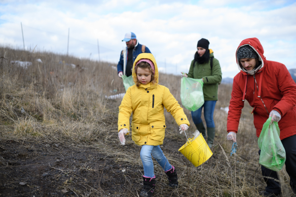 Young girl among eco activists picking up litter in nature, environmental pollution, eco activism and plogging concept.