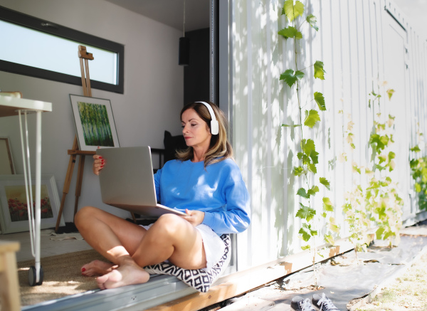 Front view of mature woman working in home office in container house in backyard.