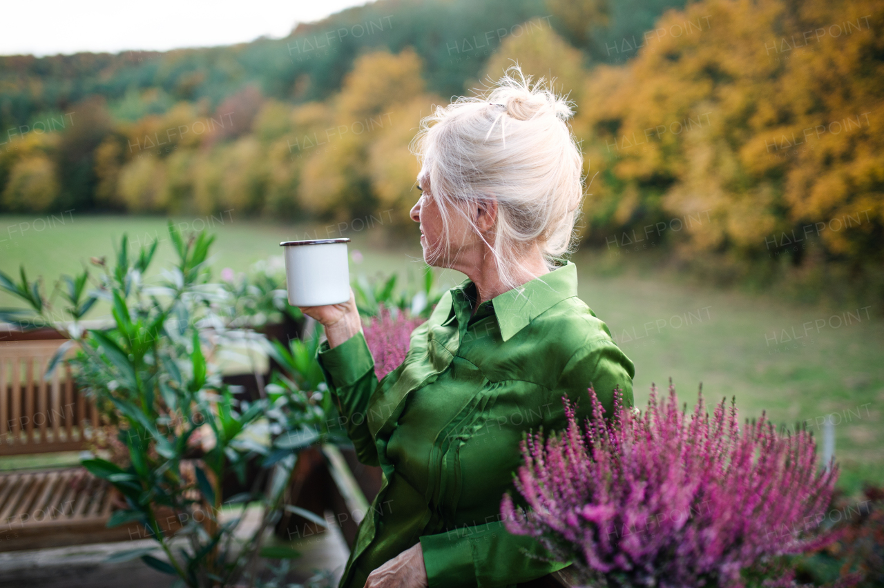 A senior woman with coffee standing outdoors on terrace, resting.