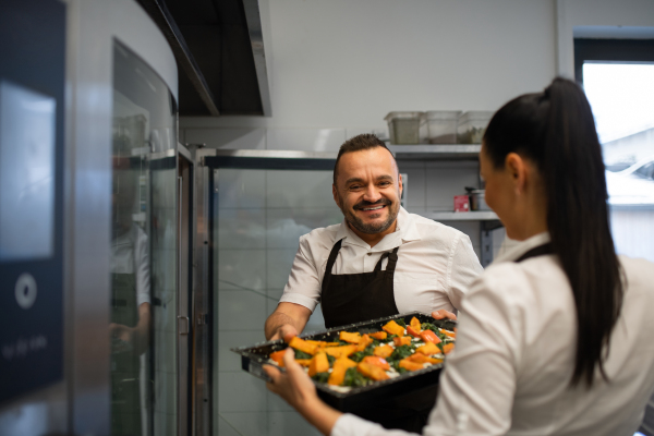A chef and cook working on their dishes indoors in restaurant kitchen.