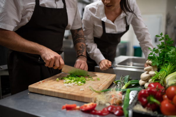 A chef teaching how to cook, cutting vegetables indoors in commercial kitchen.