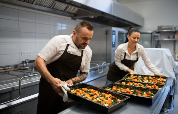 A chef and cook working on their dishes indoors in restaurant kitchen.