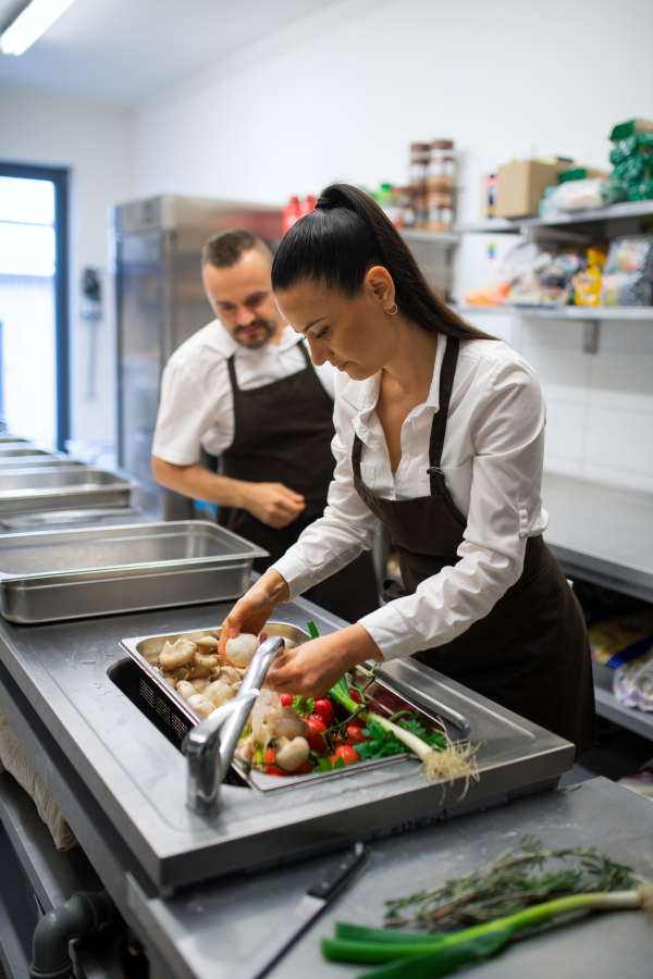 A cook washing vegetables in sink in commercial kitchen.