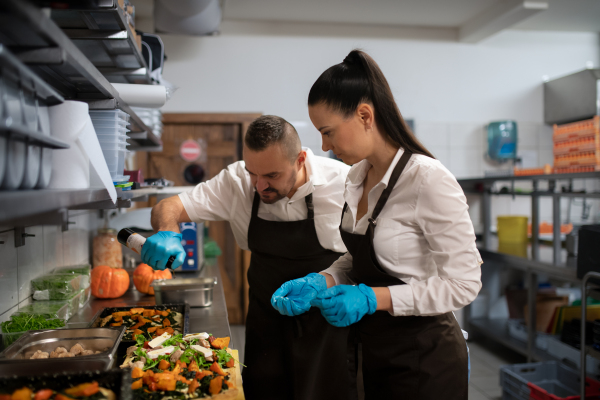 A chef and cook working on their dishes indoors in restaurant kitchen.