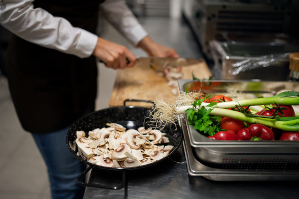 A close-up of unrecognizable chef cutting mushrooms indoors in restaurant kitchen.