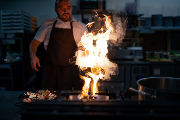 A professional chef preparing meal, flambing indoors in restaurant kitchen.