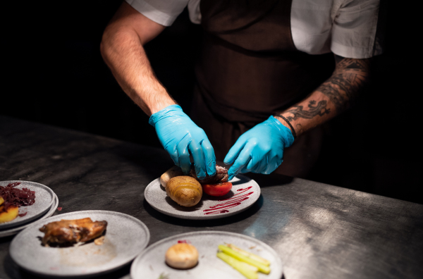 Chef's hands in gloves serving and decorating his meal in restaurant kitchen