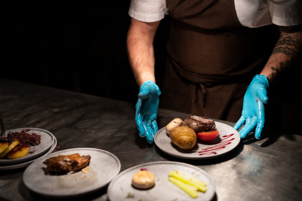 Chef's hands in gloves serving and decorating his meal in restaurant kitchen