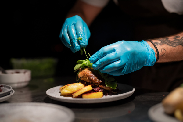 Chef's hands in gloves serving and decorating his meal in restaurant kitchen