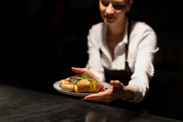 A chef handing plate with meal through order station in the commercial kitchen on black background.