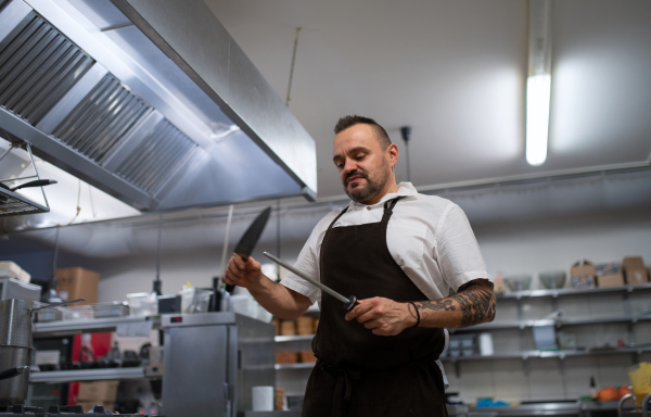 A low angle view of professional chef sharpening knife in restaurant kitchen.